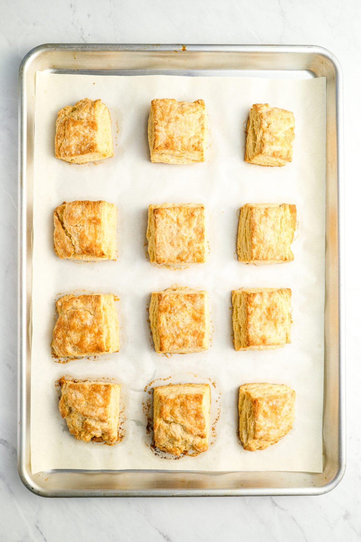 lightly golden baked buttermilk biscuits on parchment-lined baking sheet