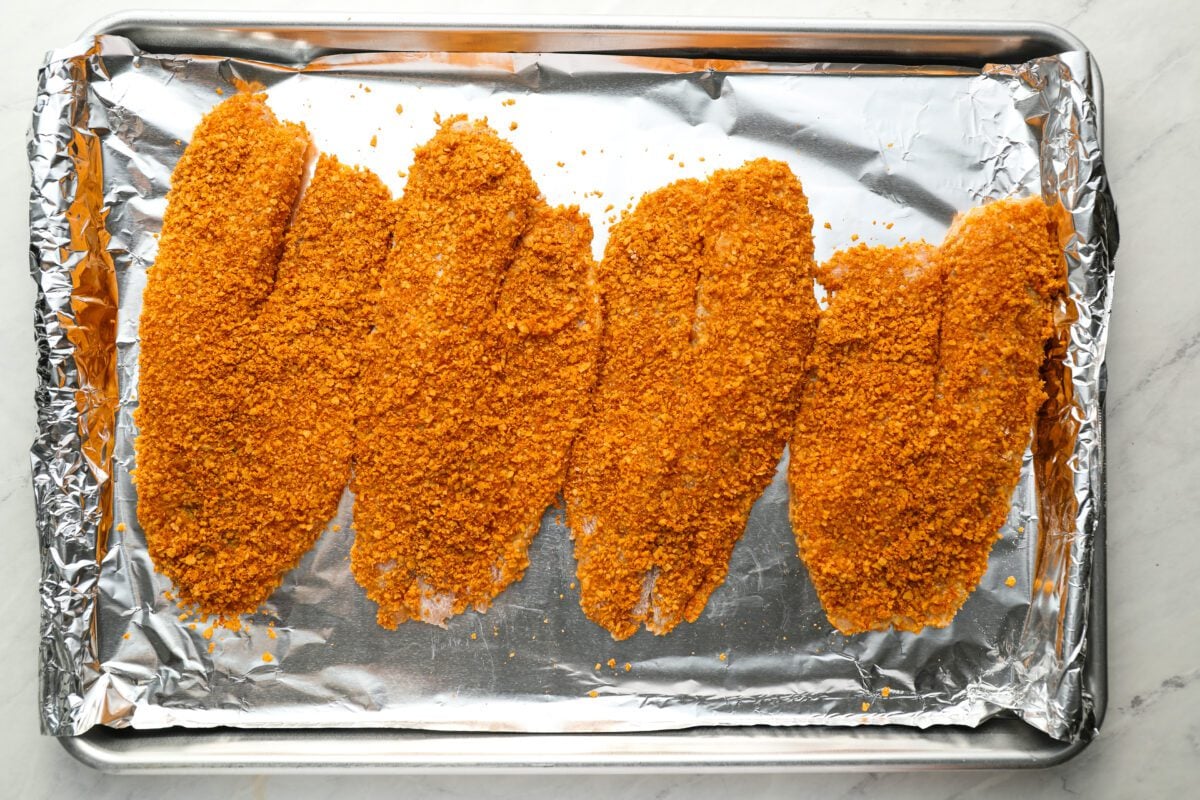 breaded tilapia fillets on a foil lined baking sheet