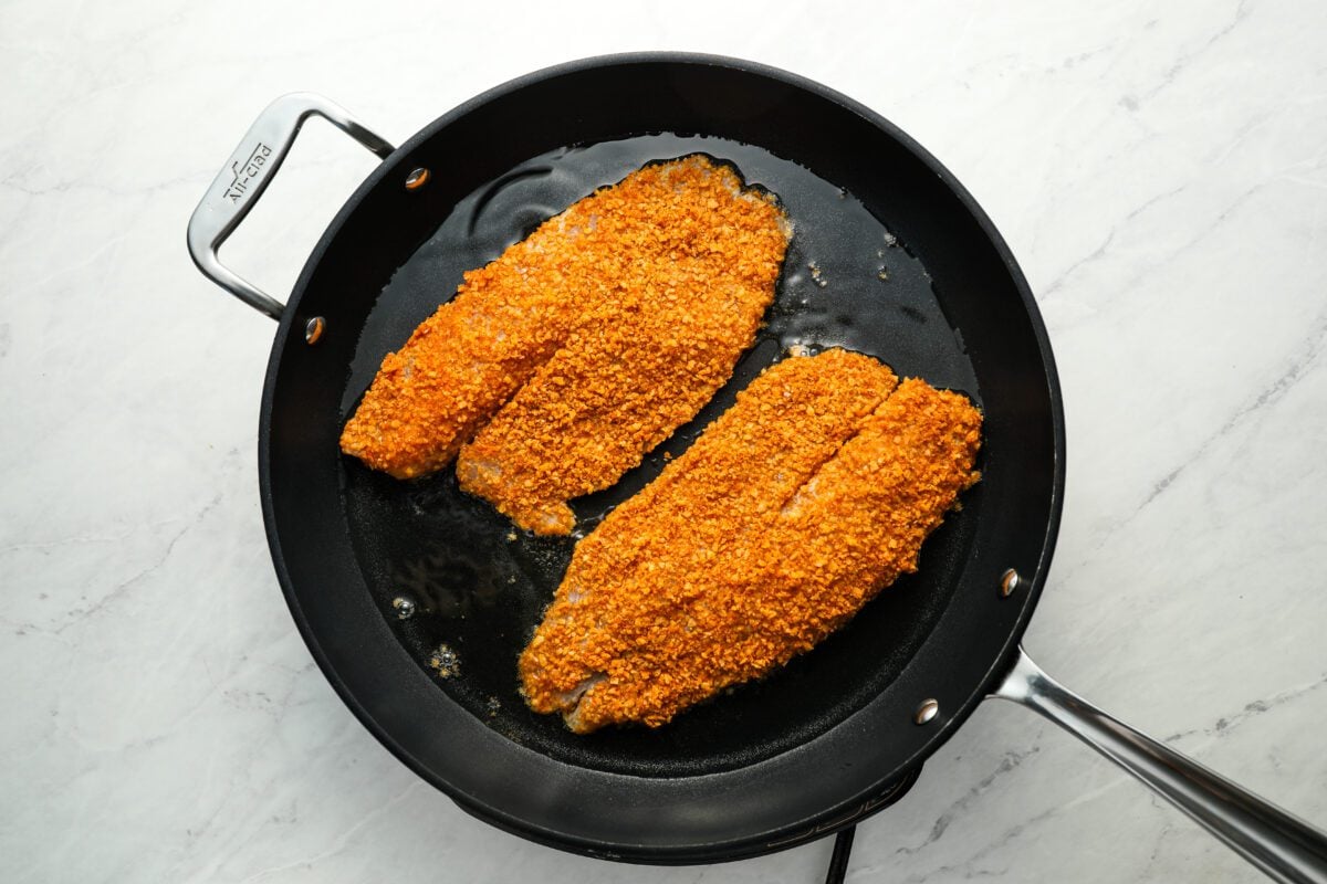 Two tilapia fillets cooking in large nonstick pan