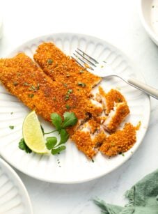 tortilla crusted tilapia on white plate with lime and cilantro