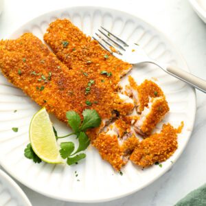 tortilla crusted tilapia on white plate with lime and cilantro