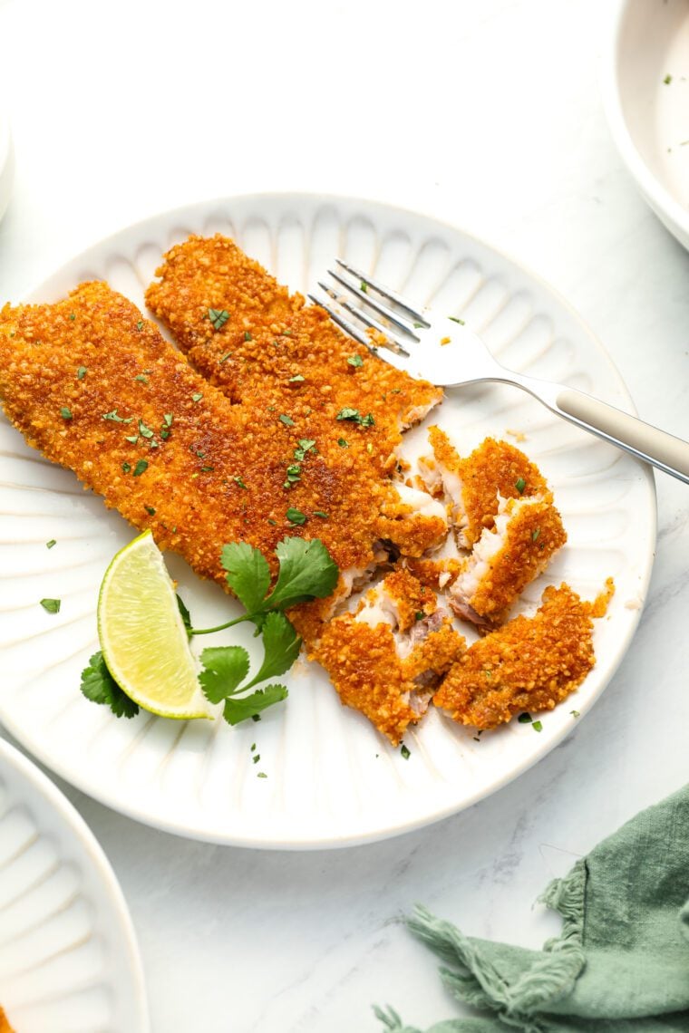 tortilla crusted tilapia on white plate with lime and cilantro