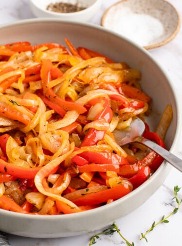 onions and peppers in bowl with salt, pepper, and thyme on side