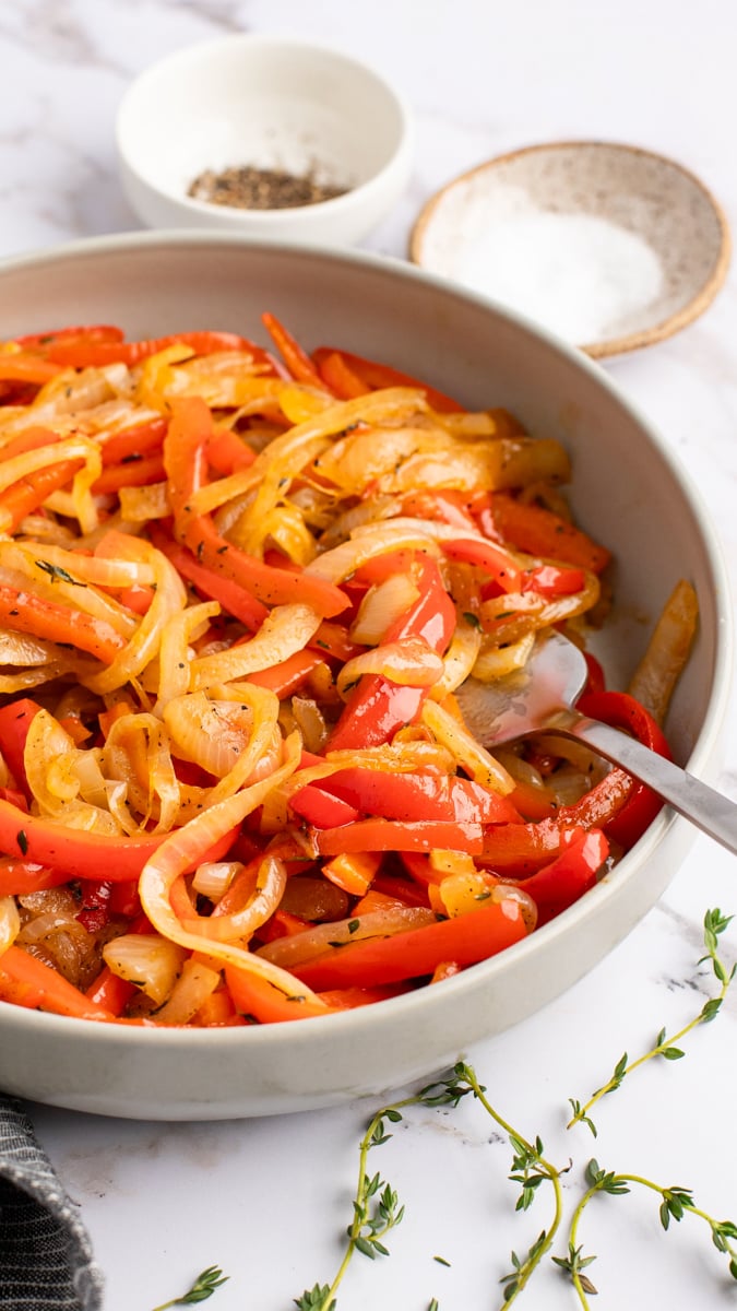 onions and peppers in bowl with salt, pepper, and thyme on side