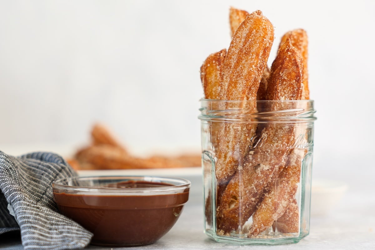 churros in glass jar with small bowl of chocolate sauce next to it