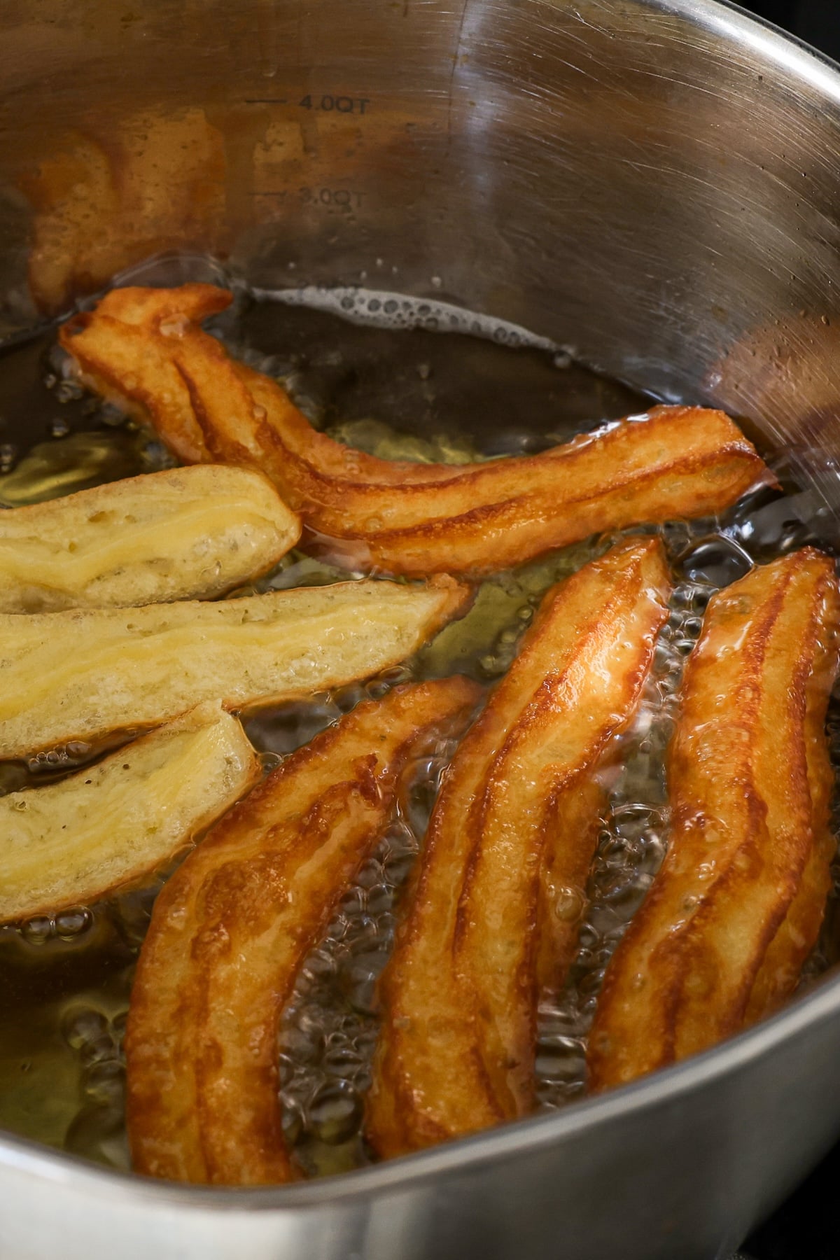 browned churros cooking in vegetable oil in heavy-bottomed pot
