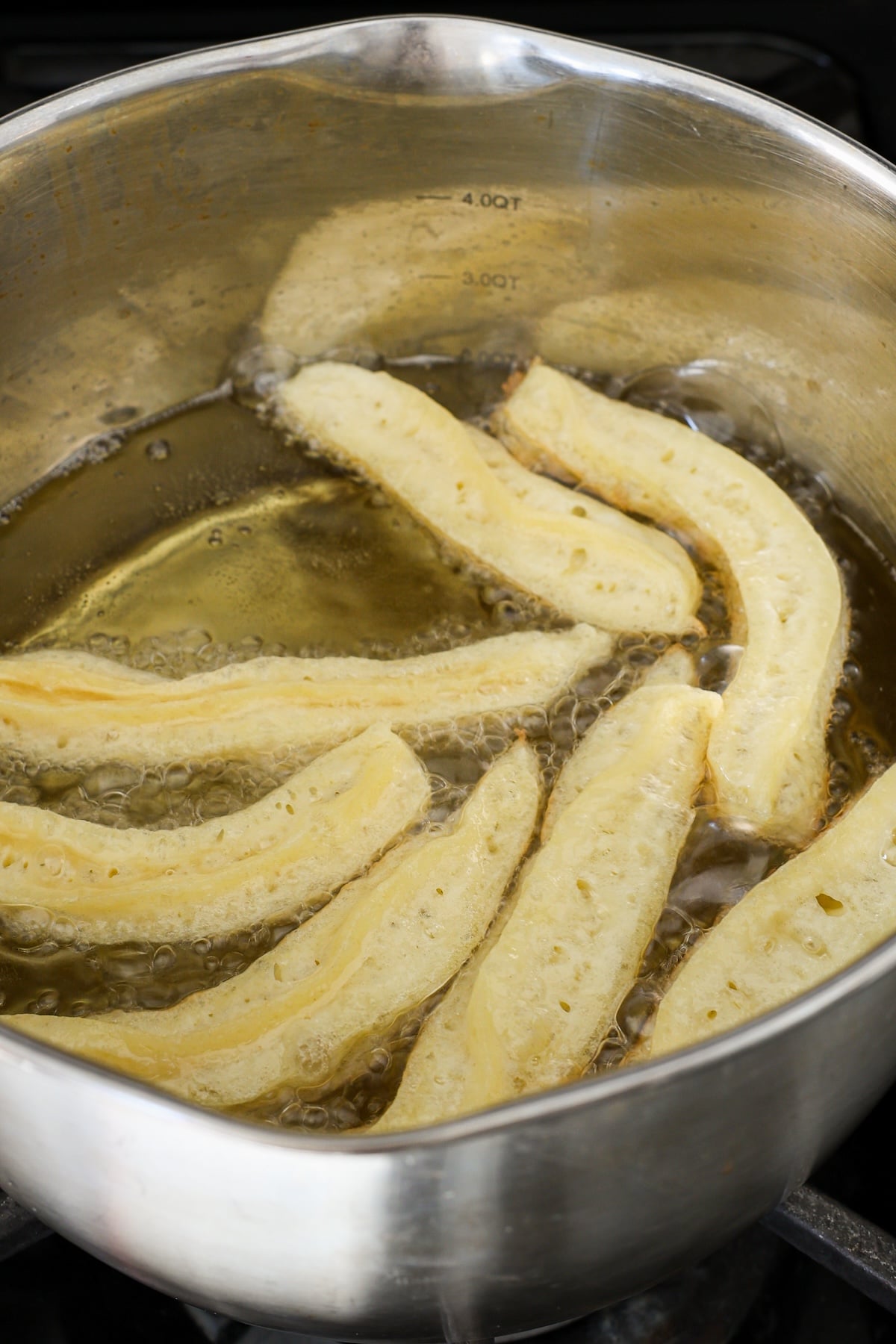 dough in churro shape frying in vegetable oil in heavy-bottomed pot