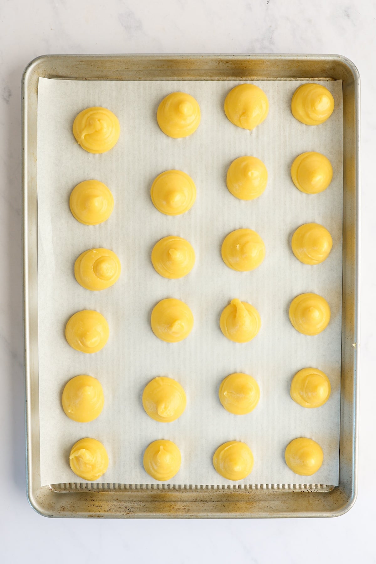 pastry mounds on parchment-lined baking sheet with dough tips pressed down.