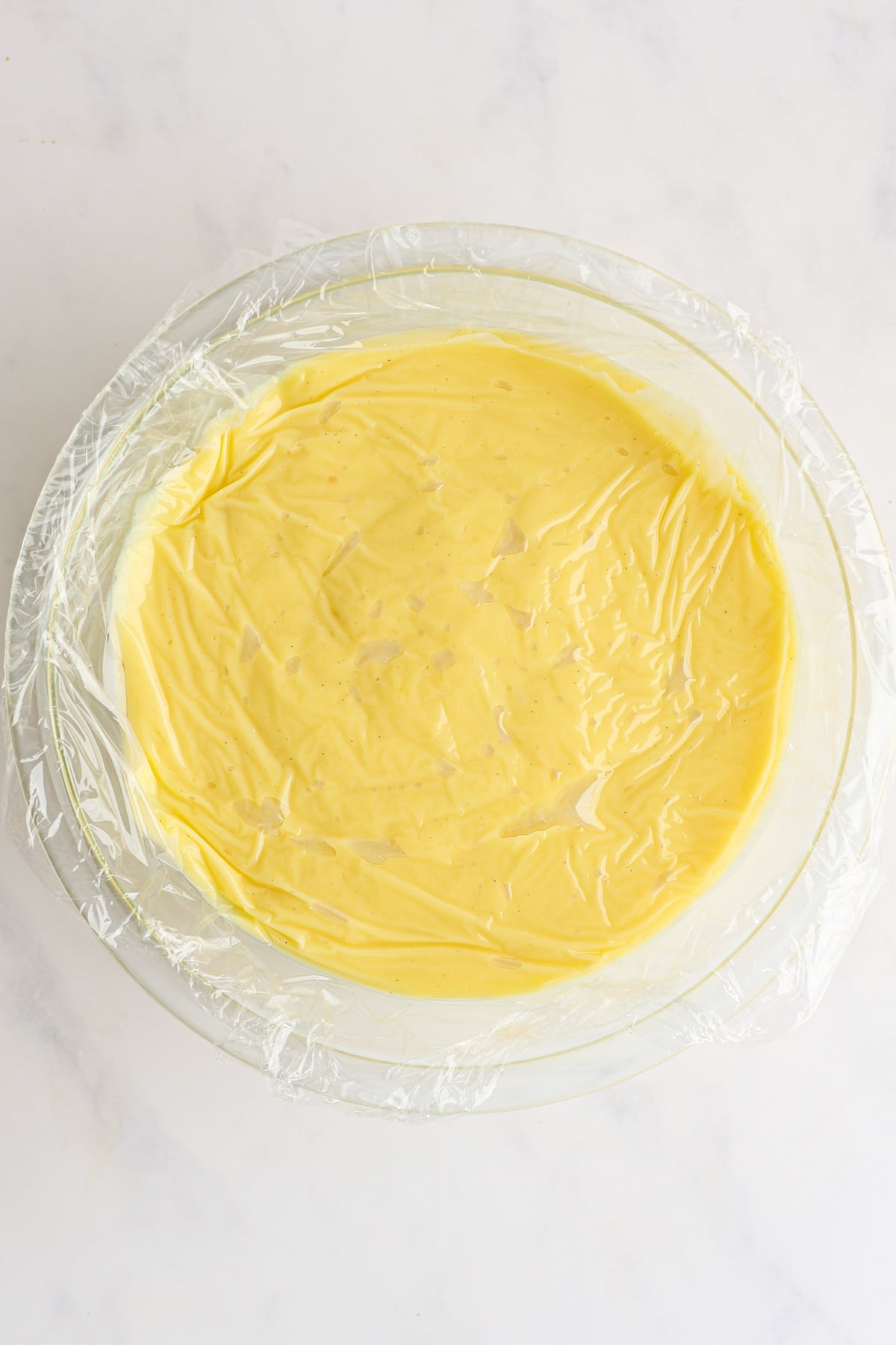 thickened mixture (pastry cream) in glass bowl plastic wrap pressed onto surface