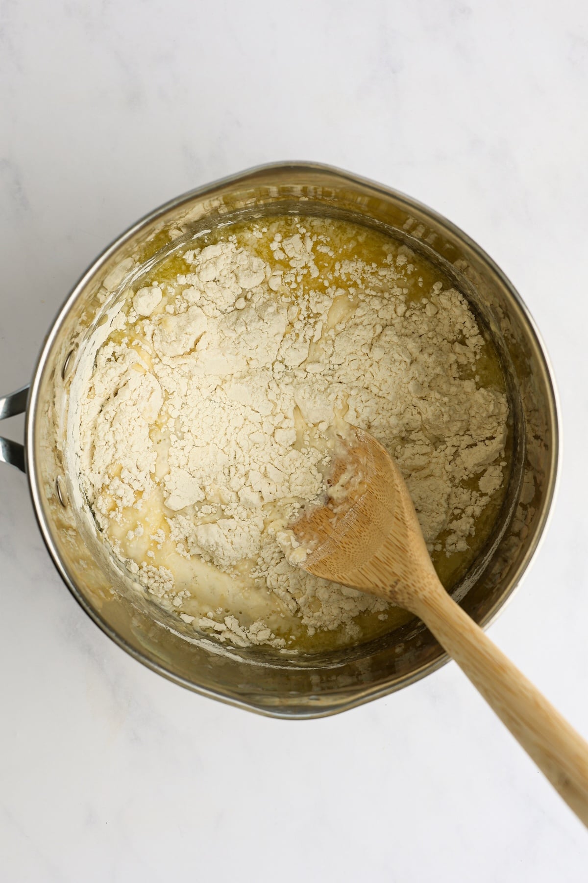 wood spoon stirring water, milk, butter, sugar, salt, and flour in medium saucepan