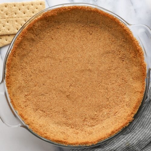 finished graham cracker crust with graham crackers, butter and sugar nearby