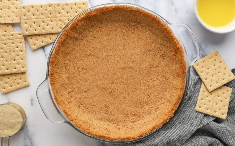 finished graham cracker crust with graham crackers, butter and sugar nearby