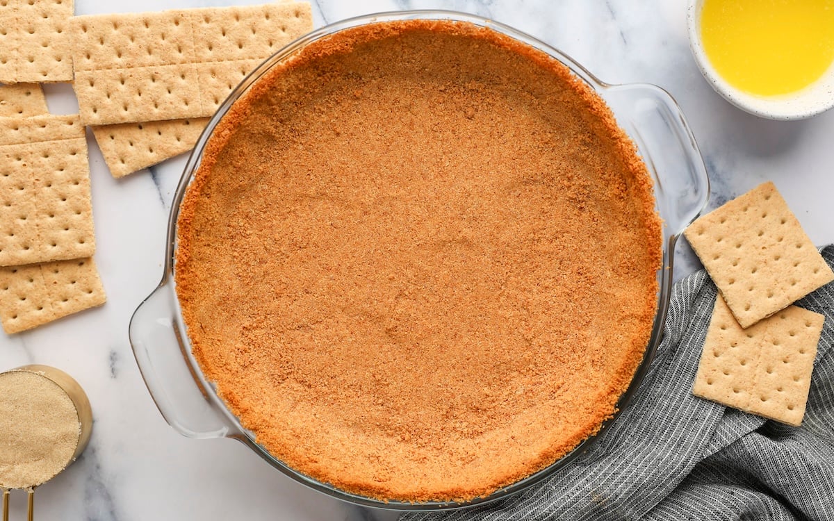baked graham cracker crust in pie plate next to graham crackers, brown sugar, and melted butter 
