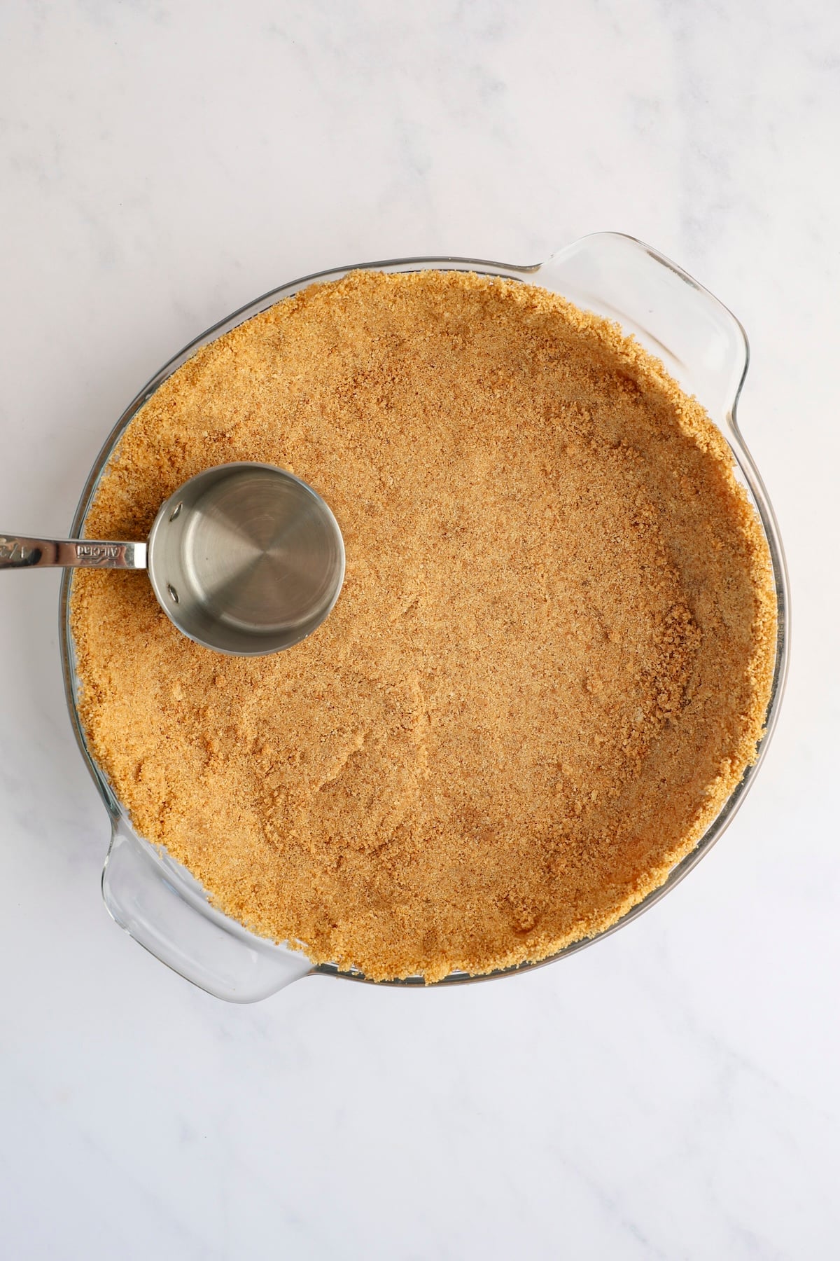 measuring cup pressing graham cracker crust crumbs evenly into pie pan