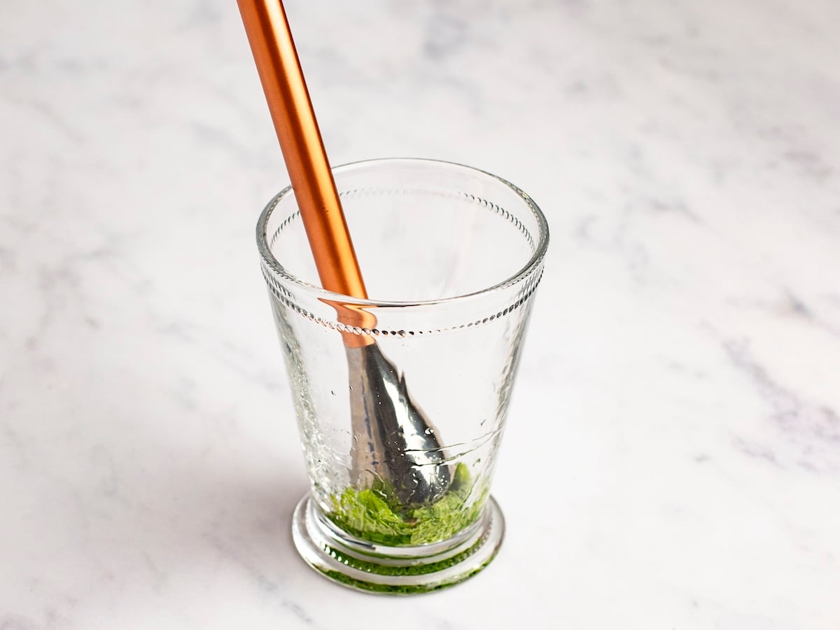 mudding mint leaves into simple syrup syrup in tall glass