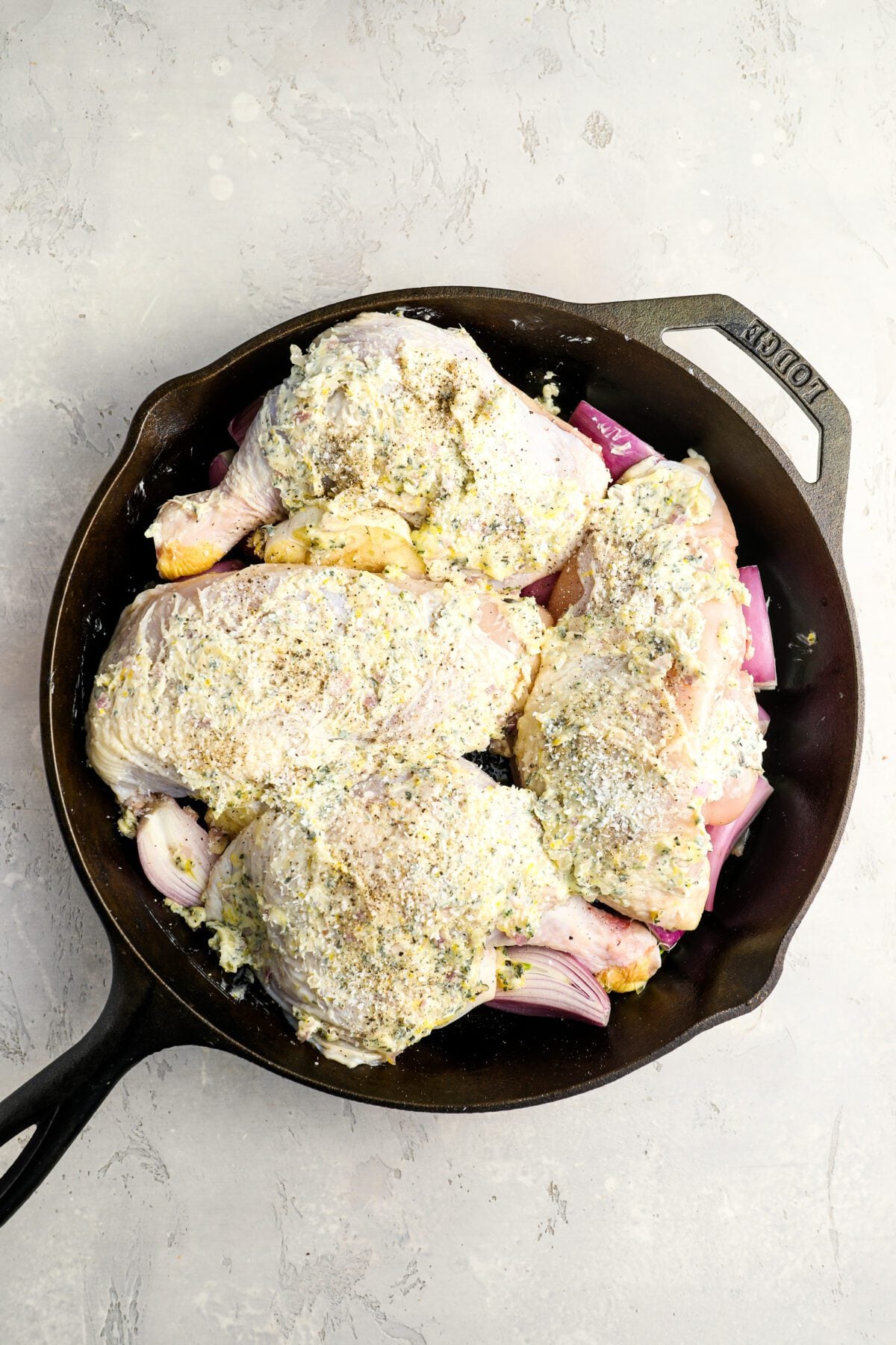 shallots, garlic, and olive oil in roasting pan topped with herb butter-covered chicken