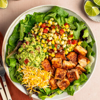 Copycat chipotle chicken in bowl with greens, corn salsa, guacamole and cheese.