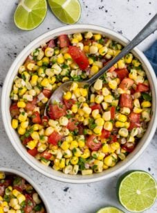 corn salsa in white bowl with limes and spoon next to bowl