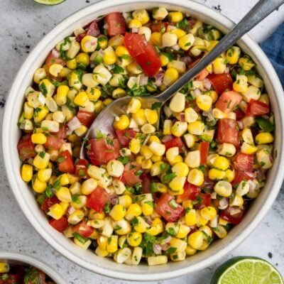 corn salsa in white bowl with limes and spoon next to bowl