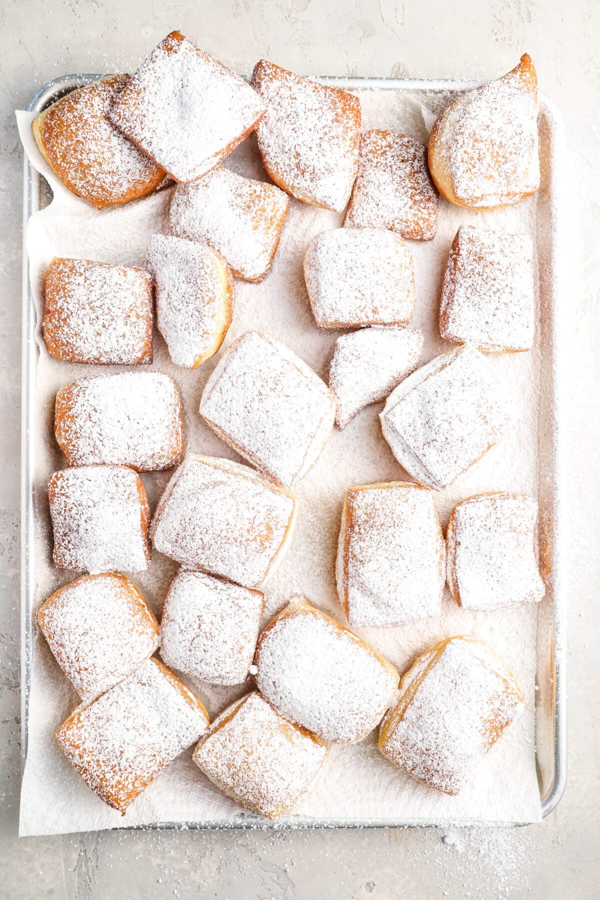 sugar-dusted golden-brown beignets on paper towel-lined baking sheet