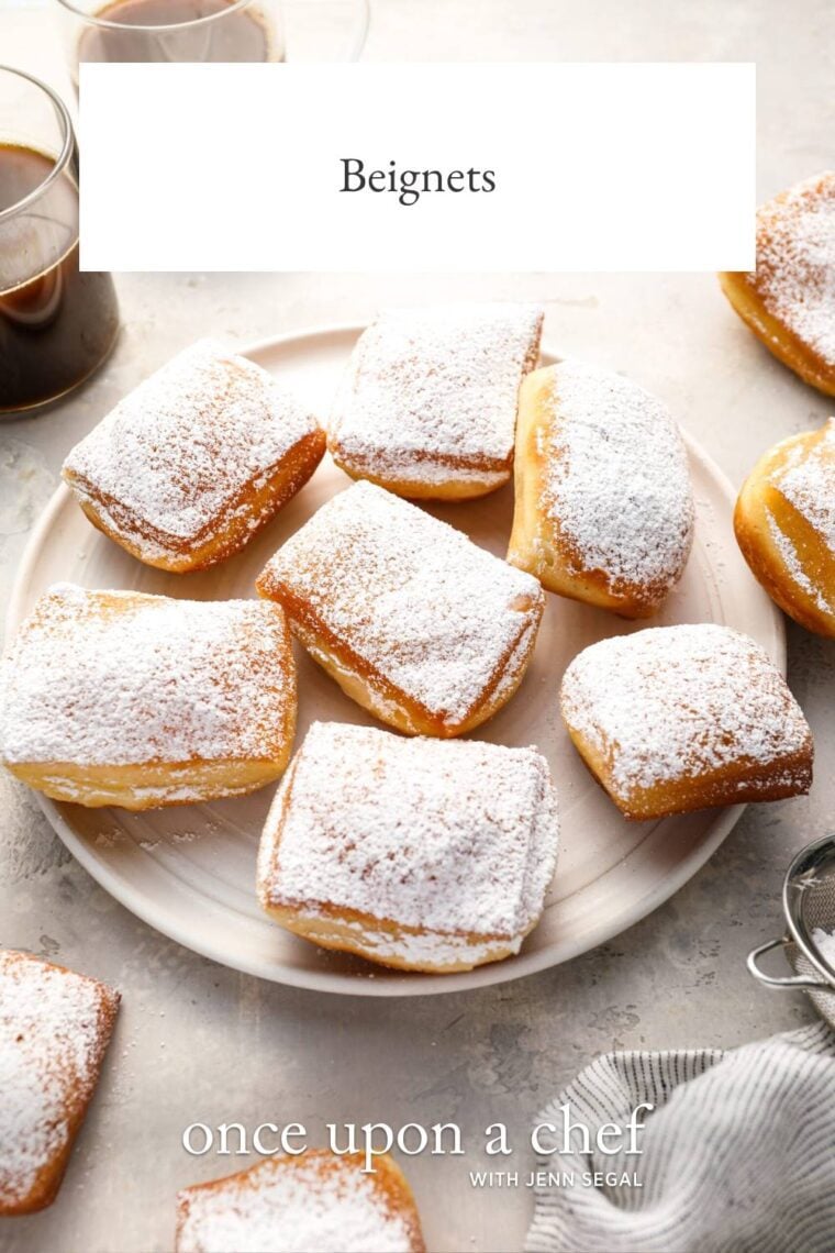 sugar-dusted beignets on white plate with 2 cups of coffee