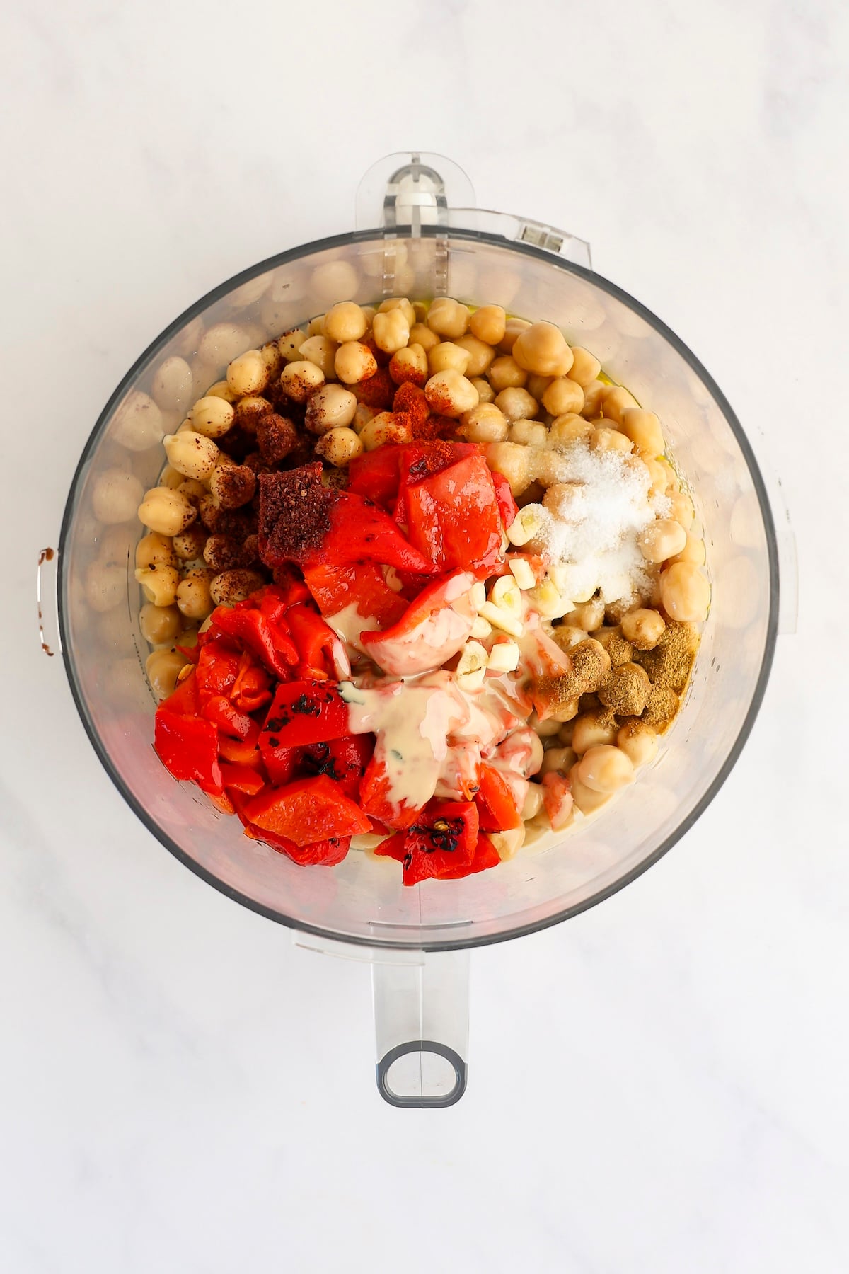 chickpeas, lemon juice, tahini, roasted red bell peppers, garlic, sumac, cumin, cayenne pepper, salt, sugar, and olive oil in bowl of food processor