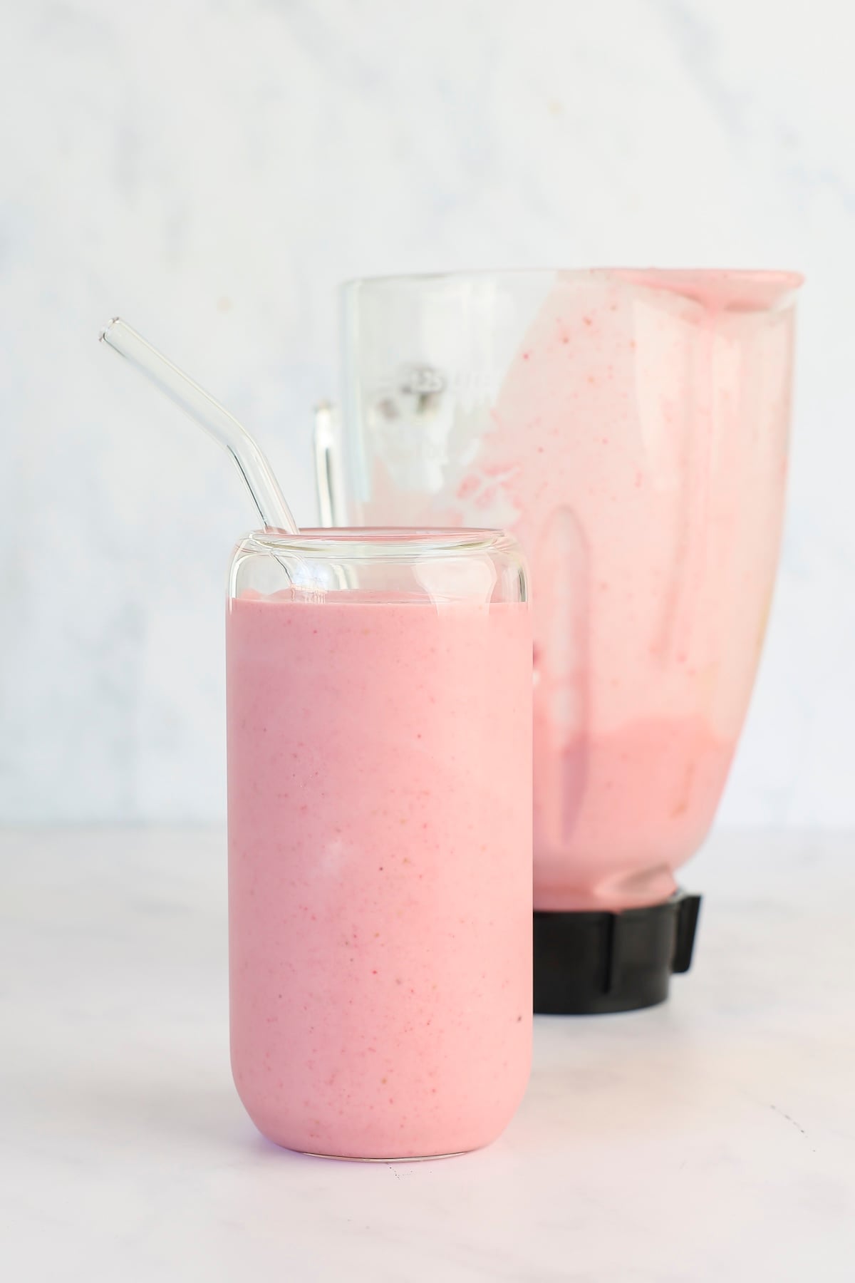 glass with straw and strawberry banana smoothie; blender in background
