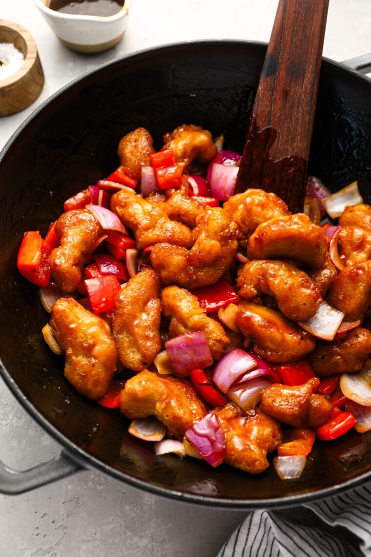 sweet and sour chicken in wok with wooden spoon and striped linen napkin