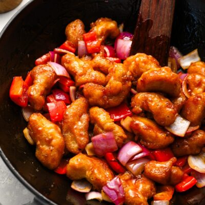 sweet and sour chicken in wok with wooden spoon and striped linen napkin