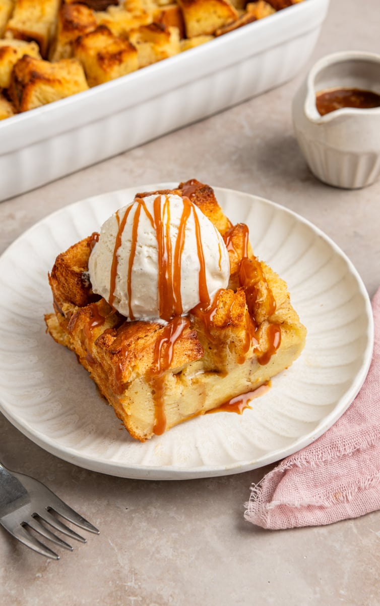 slice of bread pudding on plate topped with vanilla ice cream and caramel sauce