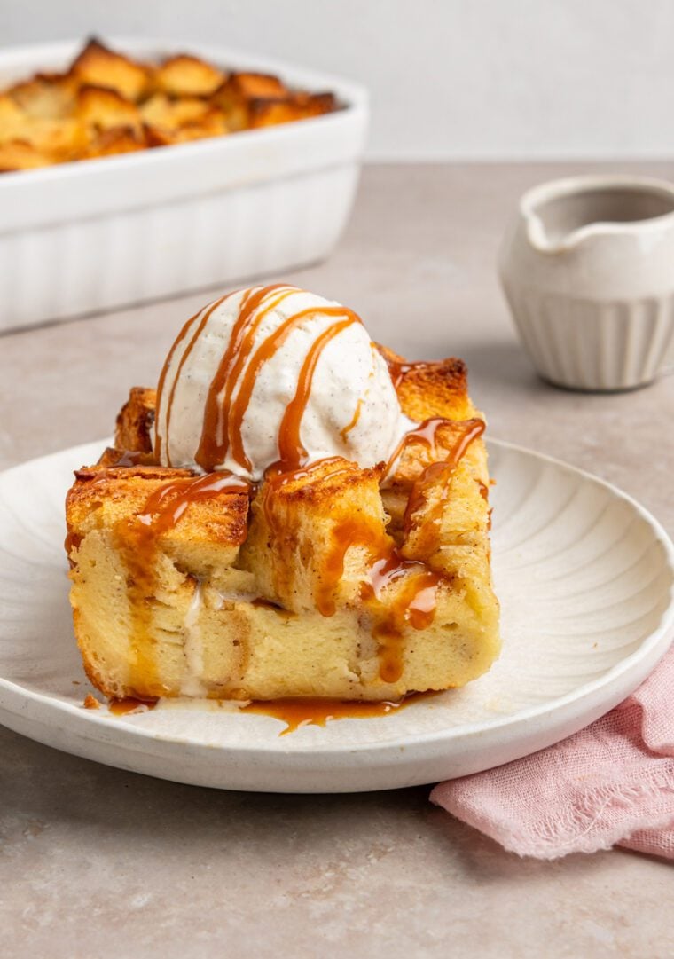 slice of bread pudding on plate topped with vanilla ice cream and caramel sauce