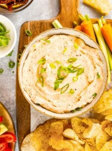 Sun-dried tomato dip in serving bowl on wood cutting board