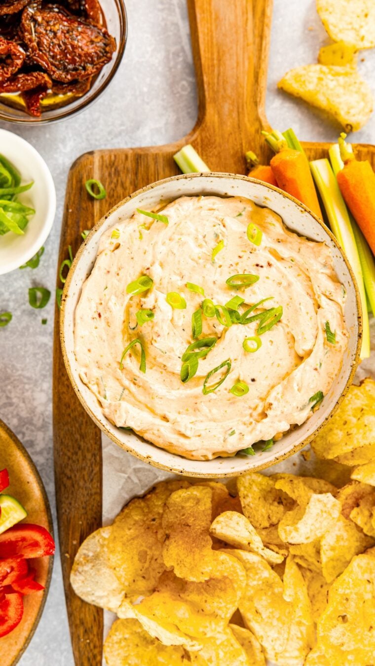 Sun-dried tomato dip in serving bowl on wood cutting board