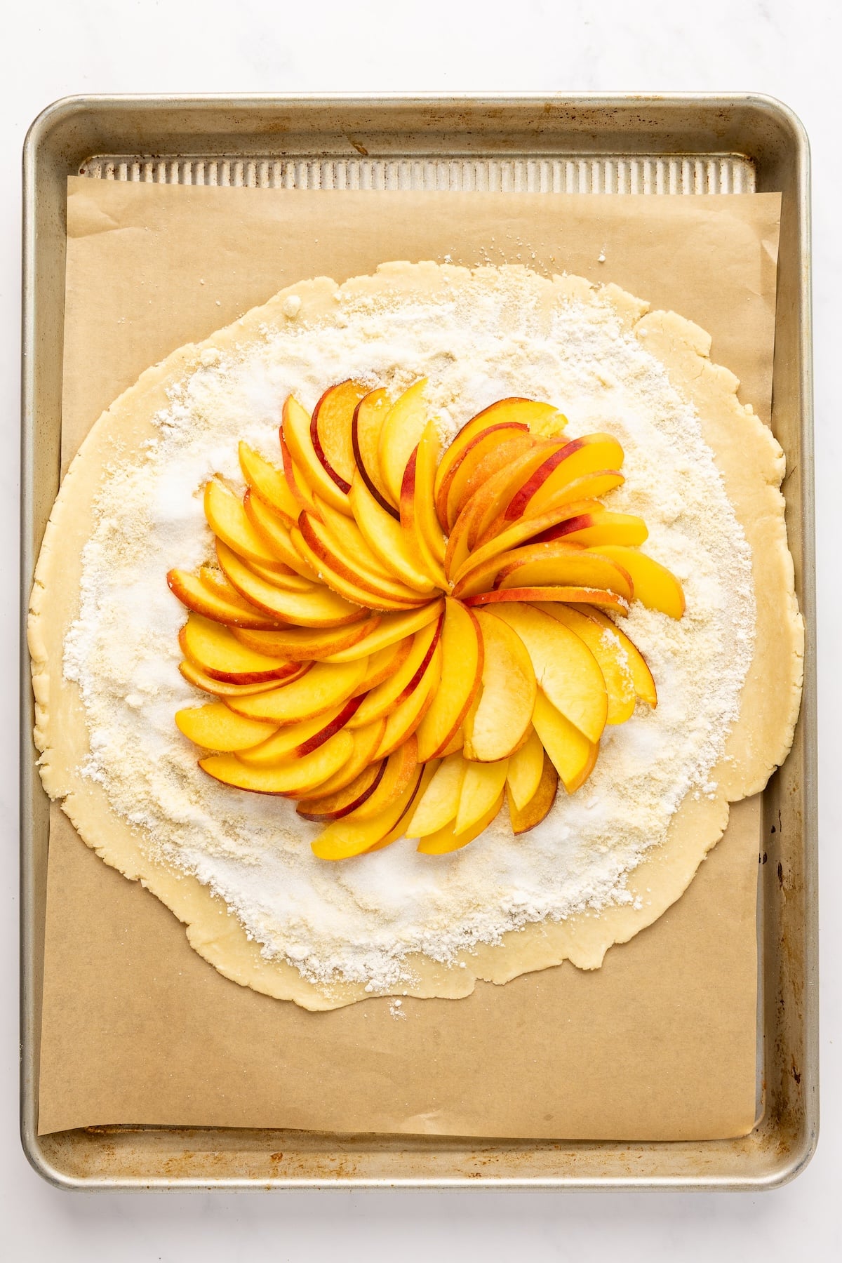 13-inch dough disk topped with layer of all purpose flour, almond flour, granulated sugar and peaches fanned in circle