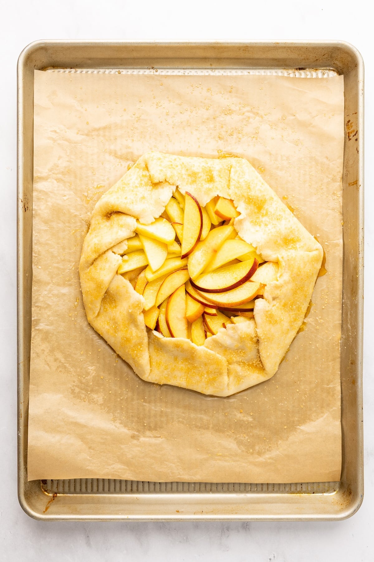 fully assembled unbaked peach galette on parchment-lined baking sheet 