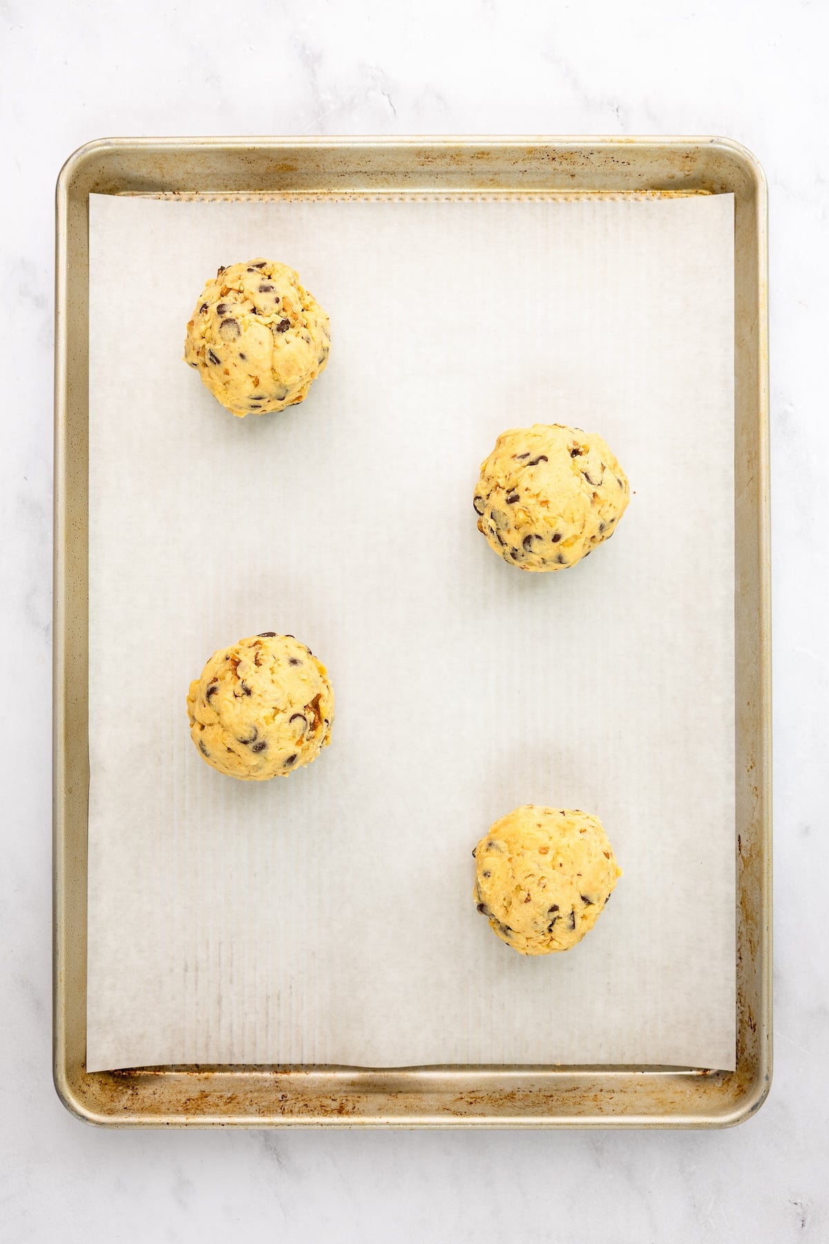 parchment-lined baking sheet with 4 balls of cookie dough