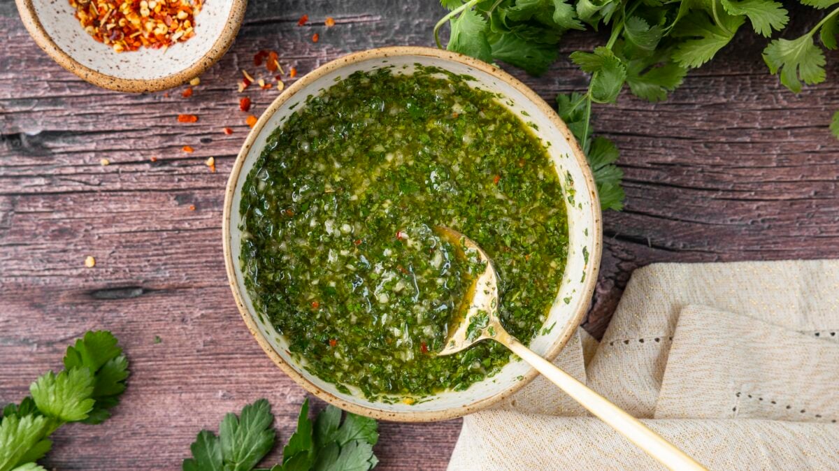 tan bowl with chimmichurri sauce sitting on rustic wood table