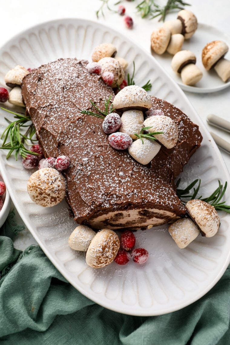 yule log cake on platter decorated with meringue mushrooms and sugared cranberries