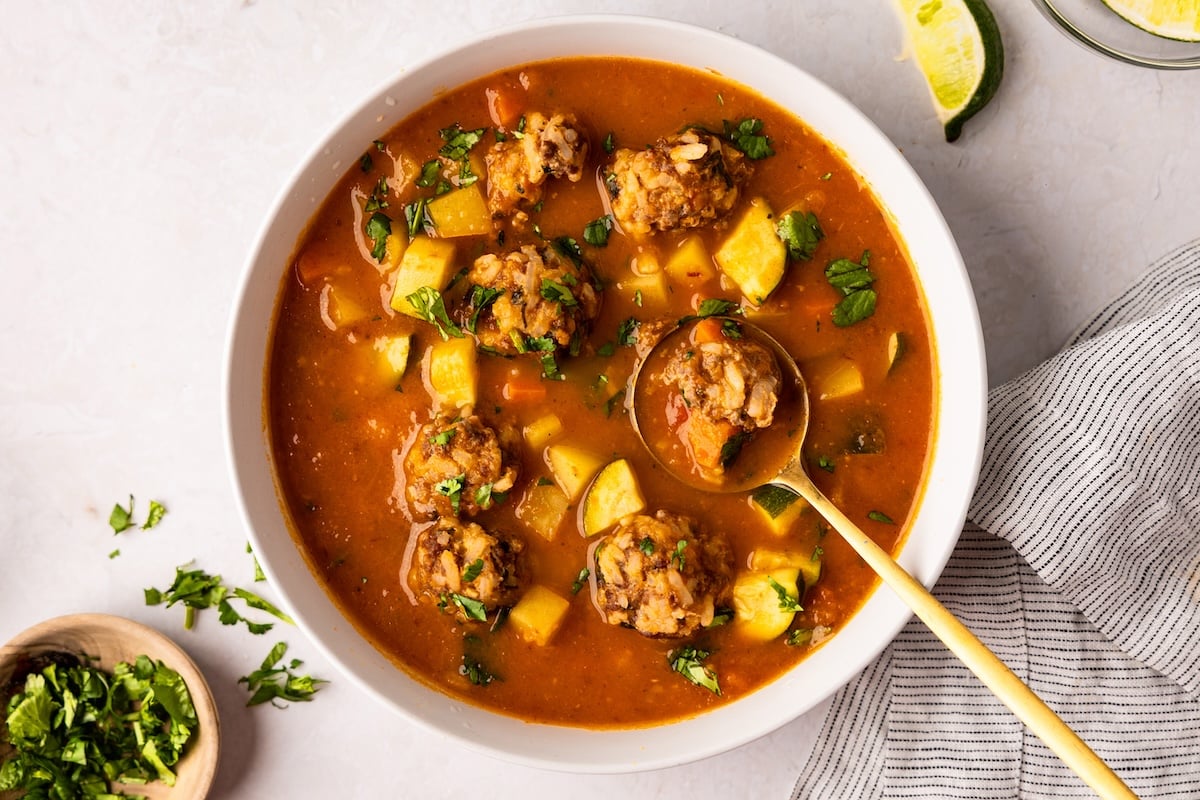 albondigas soup in white bowl with lime wedges and cilantro nearby