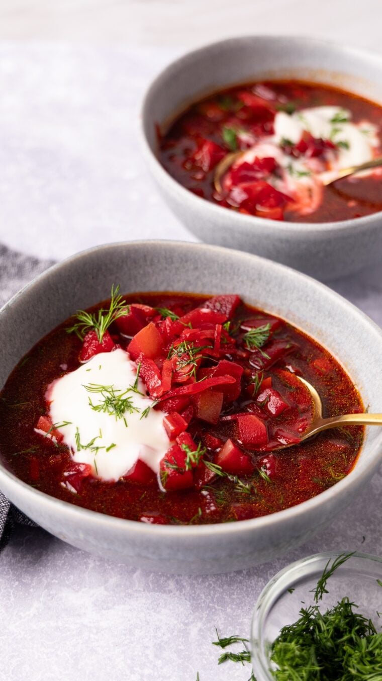 2 bowls of borscht topped with sour cream and fresh dill