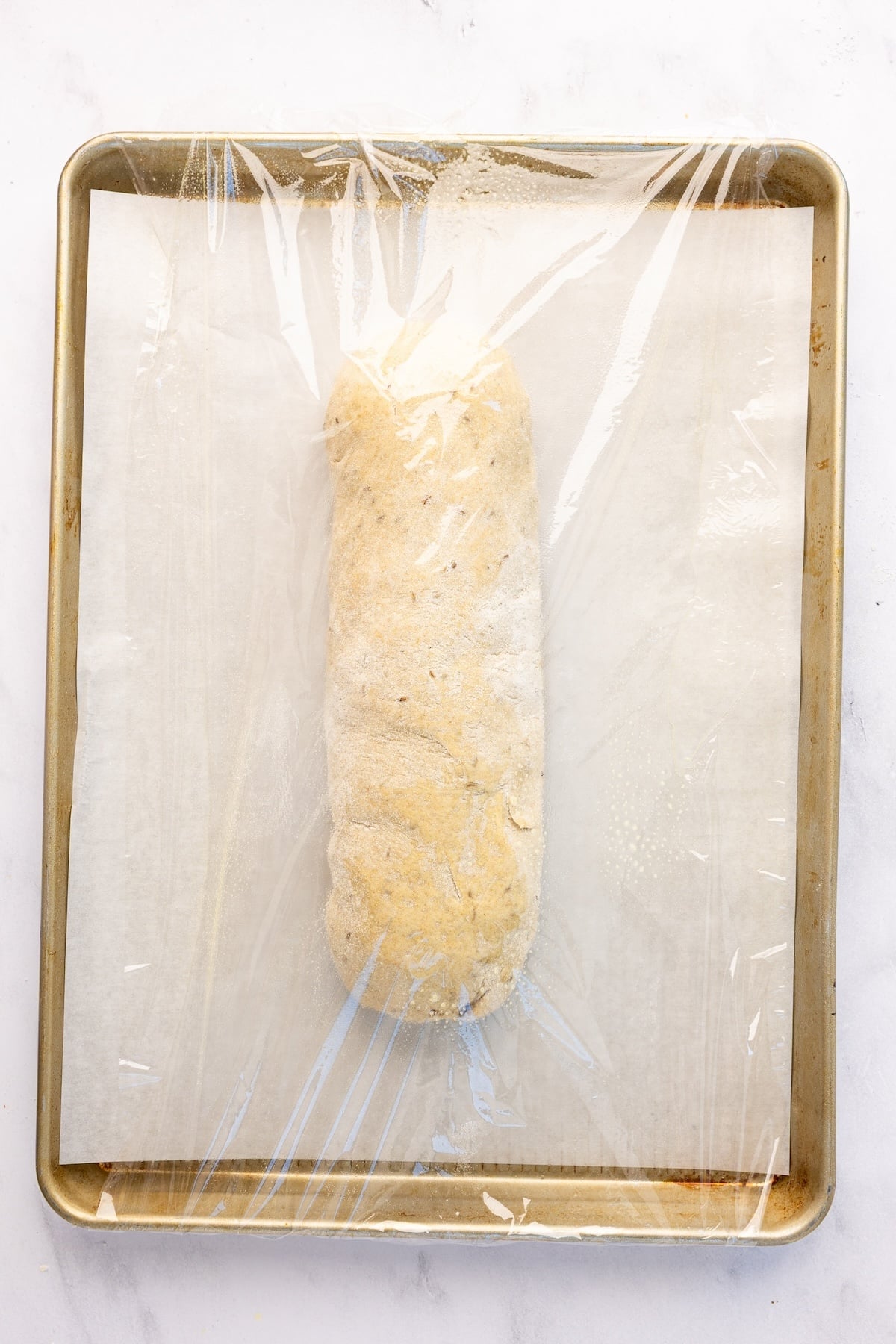 rye loaf on parchment lined baking sheet covered with plastic wrap 