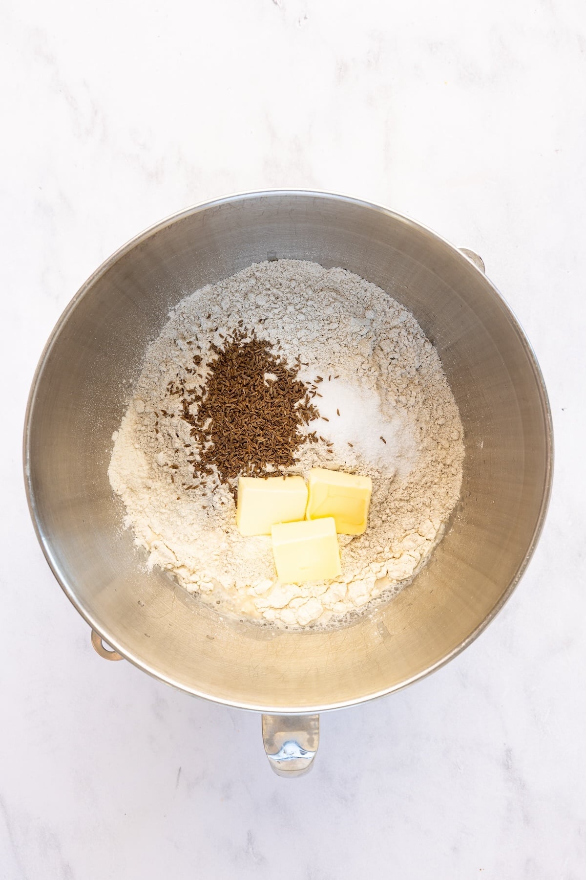 mixing bowl with salt, bread flour, rye flour, caraway seeds, and butter added to the water/honey mixture