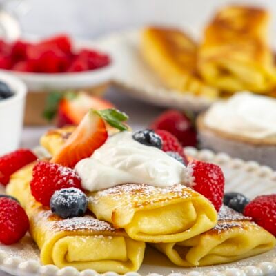 Cheese blintzes stacked on plate with sour cream and berries