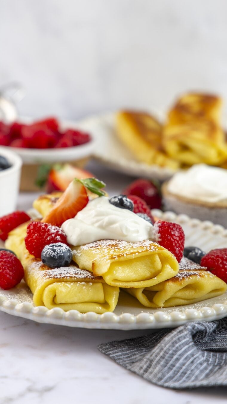 Cheese blintzes stacked on plate with sour cream and berries