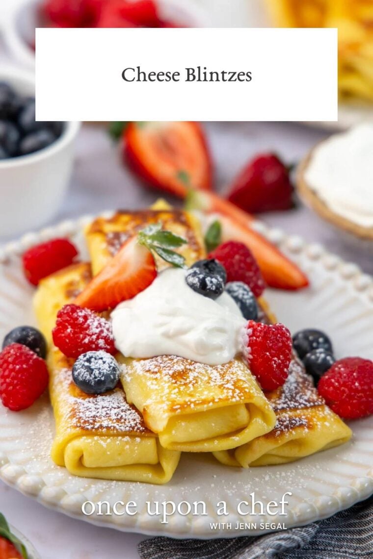 white plate with 3 cheese blintzes topped with sour cream, confectioners' sugar, and fresh berries