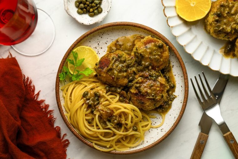 Chicken piccata meatballs with pasta and a glass of red wine.