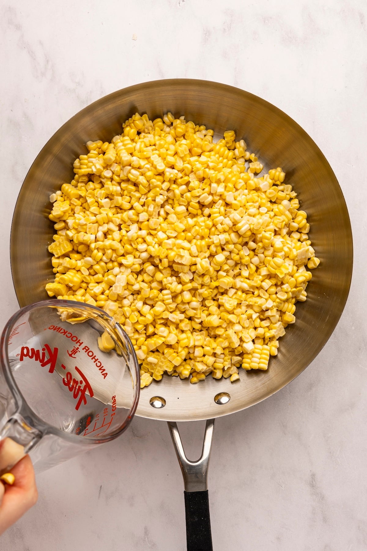 pouring water into large skillet with corn kernels
