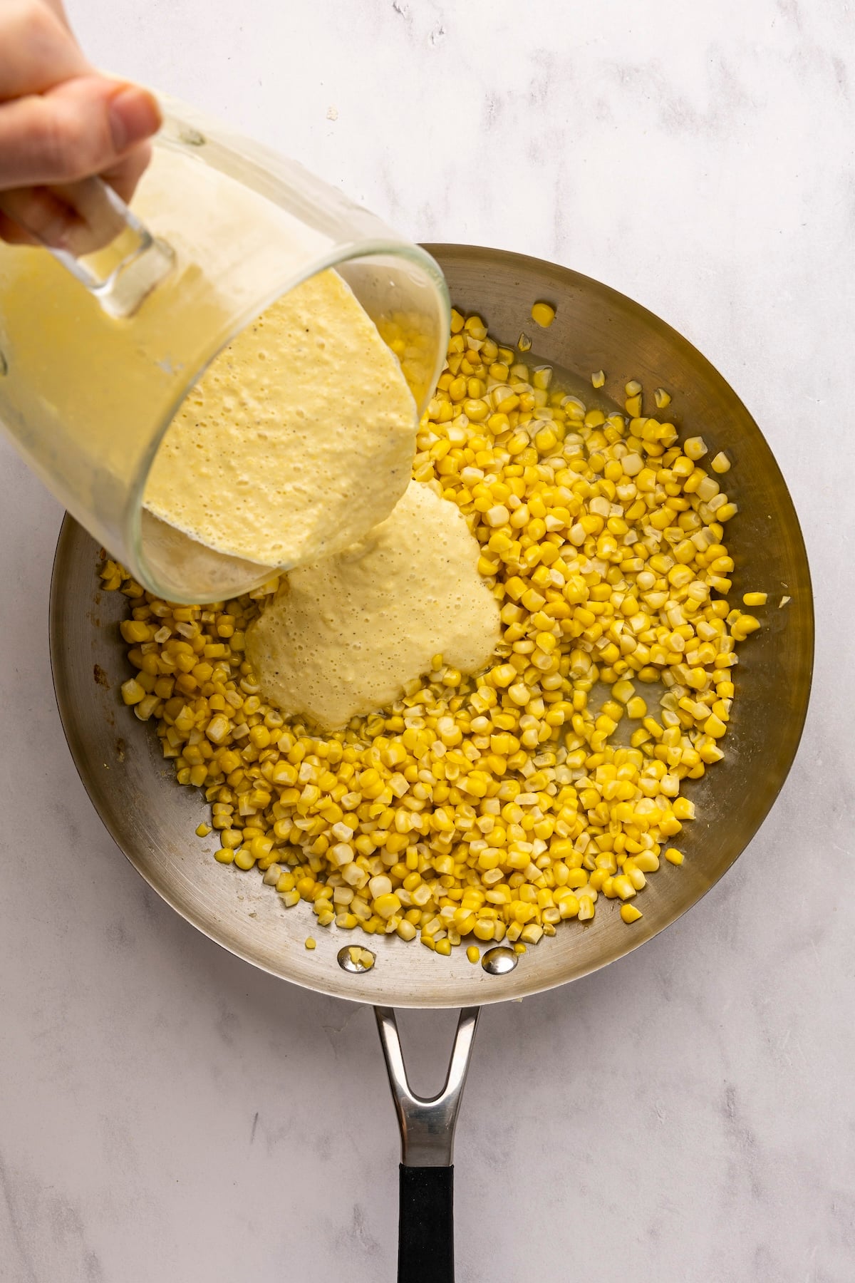pouring corn puree into large skillet with corn kernels