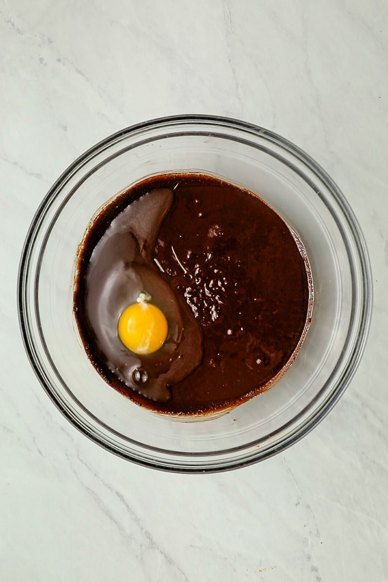 Egg added to brownie filling in glass bowl.
