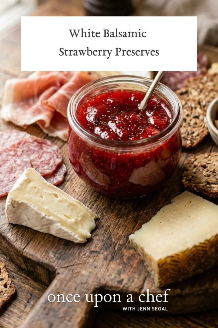 wood board with wedges of cheese, prosciutto, and jar of white balsamic strawberry preserves